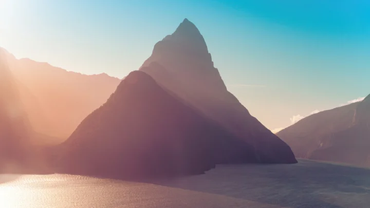 薄い霧を通した陽光が、静かな湖畔のそびえ立つ山を照らしている。