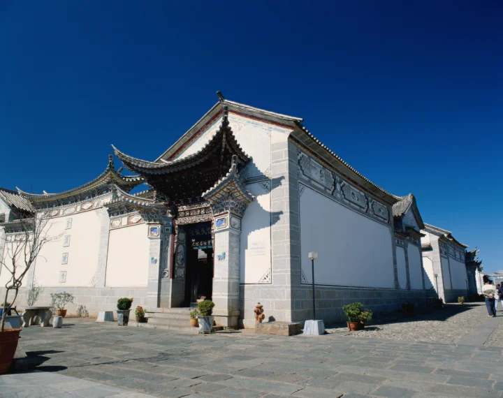 蓝天下，一座白墙灰瓦的传统中式古建筑围绕着石板庭院展开。