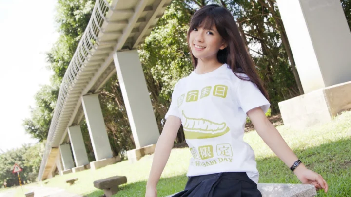 一位长发女子在阳光明媚的户外绿地旁微笑着面对镜头。