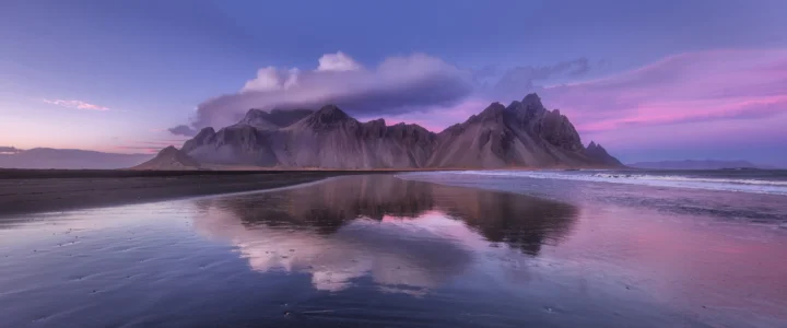 紫色暮光映照着海岸山脉，潮湿沙滩倒映出天空与群山。