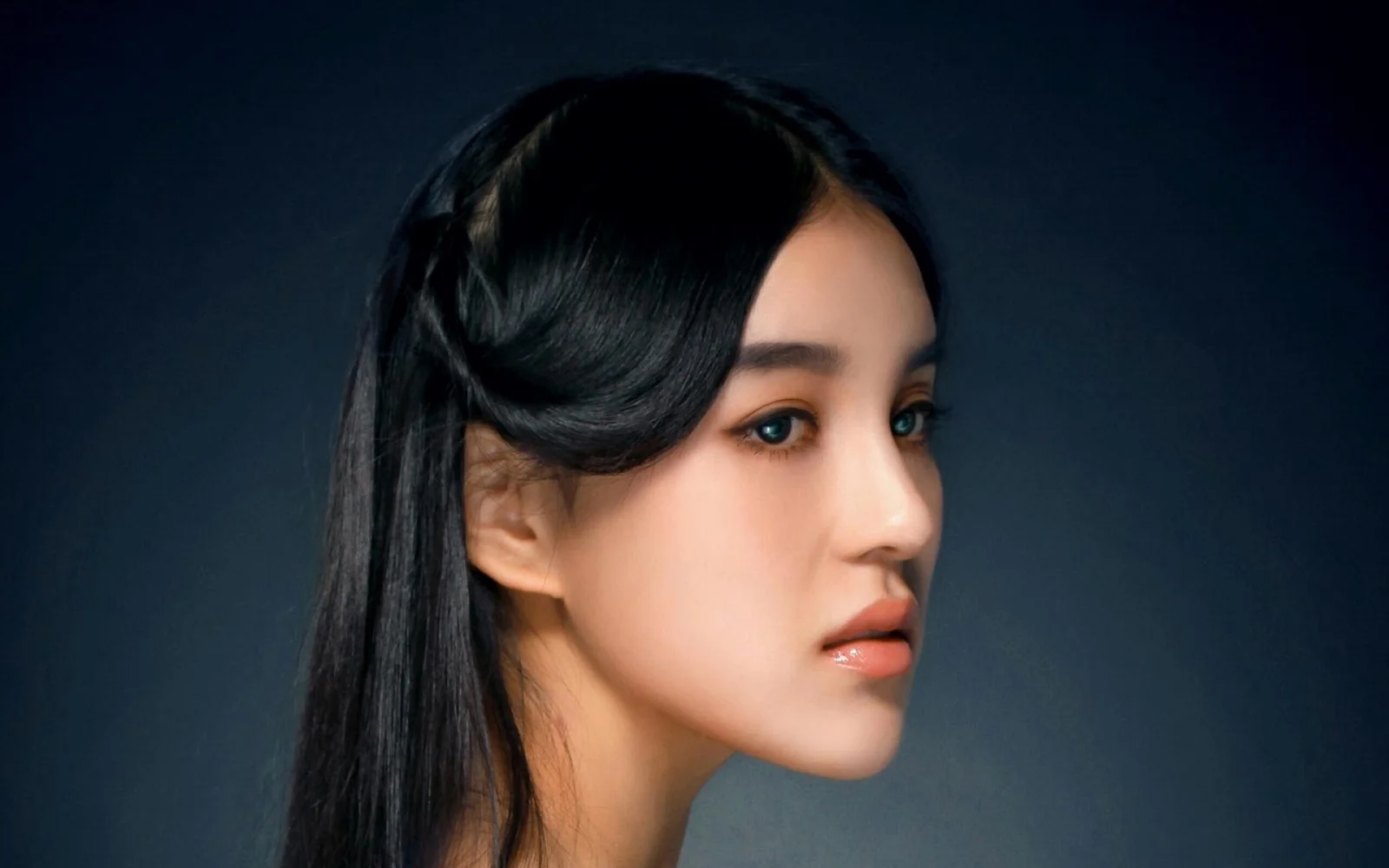 어두운 배경 앞에서 검은 머리의 성인 여성이 오른쪽을 향한 옆모습을 보이고 있습니다.