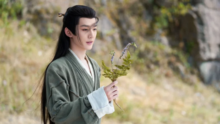 一名身穿传统服饰的男子在户外手持一束小花。