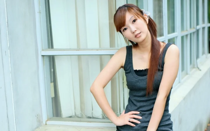 一名长发女性穿着深色背心坐在窗边。