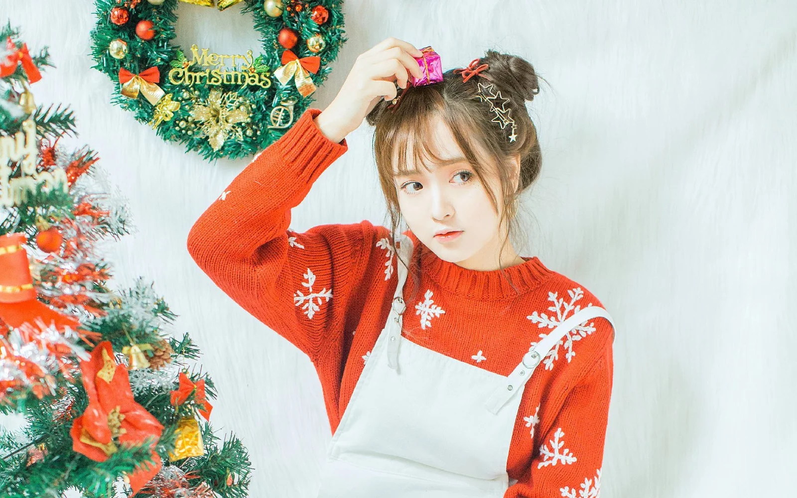 一名成年女性穿著紅色聖誕毛衣站在聖誕樹旁。