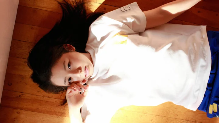 白いトップスを着た女性が、日差しの差し込む木の床に横たわっています。