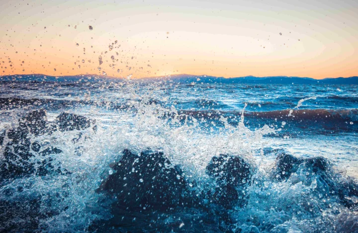 夕阳映照下，海浪在近岸翻涌并溅起大片水花。