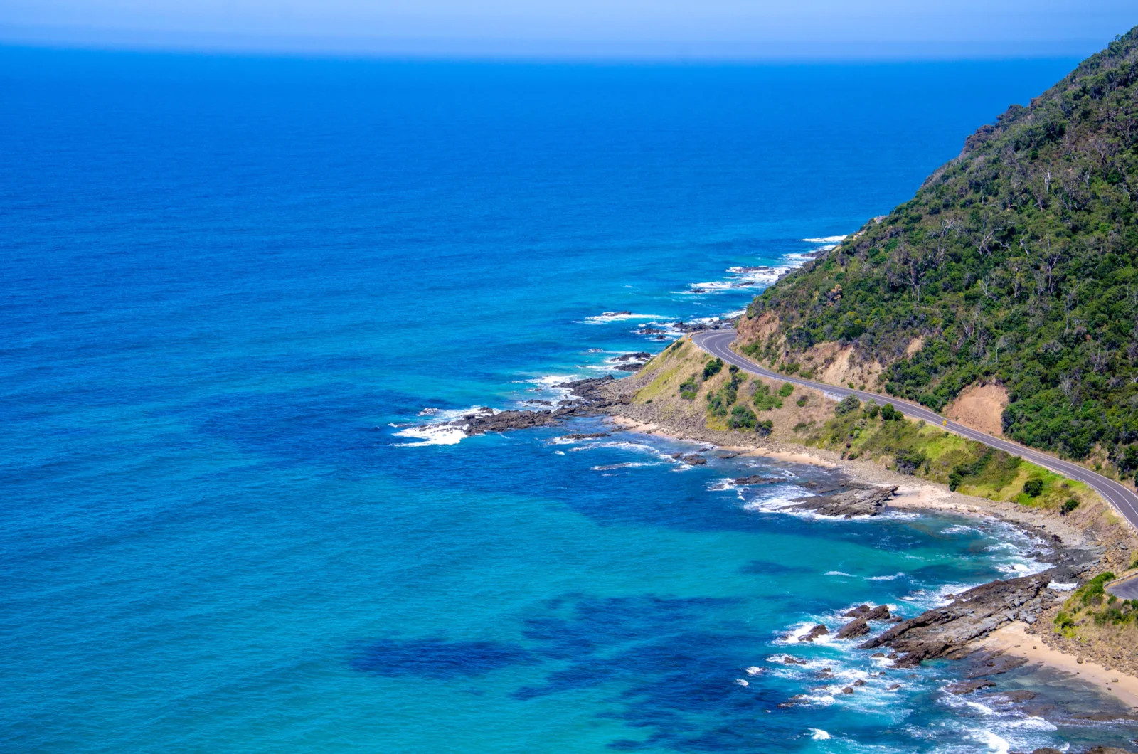 湛蓝海水沿着植被覆盖的海岸延伸，一条蜿蜒公路穿过山坡。