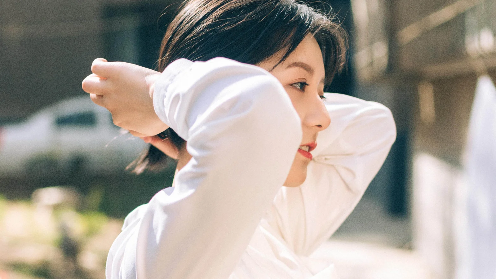 一位身穿白色长袖上衣的女性在明亮的户外光线下整理头发。