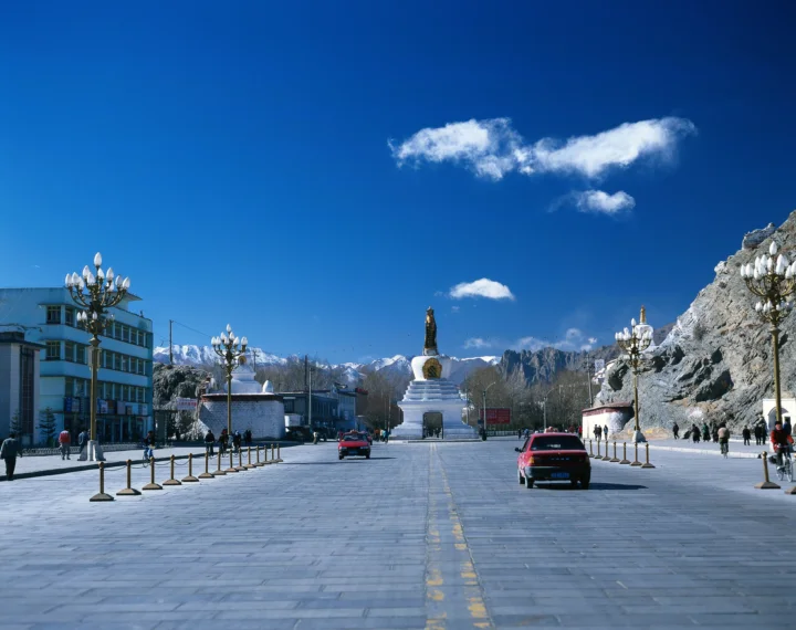 宽阔的城市广场中央矗立着纪念碑，远处是雪山和蓝天。