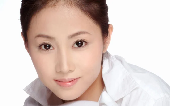 一名成年女性身穿白色衣领上衣，在白色背景前进行近距离肖像拍摄。