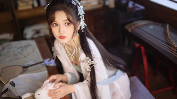 一名身穿浅色传统服饰的女子坐在室内弦乐器旁。