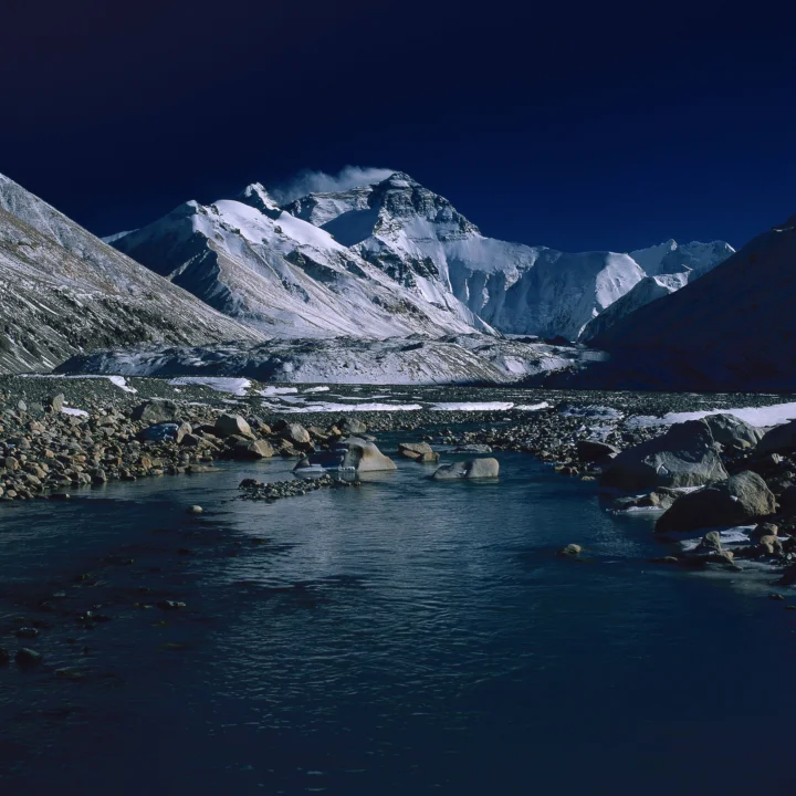 雪山与冰川映衬着深蓝天空，前景是一条流经岩石的河流。