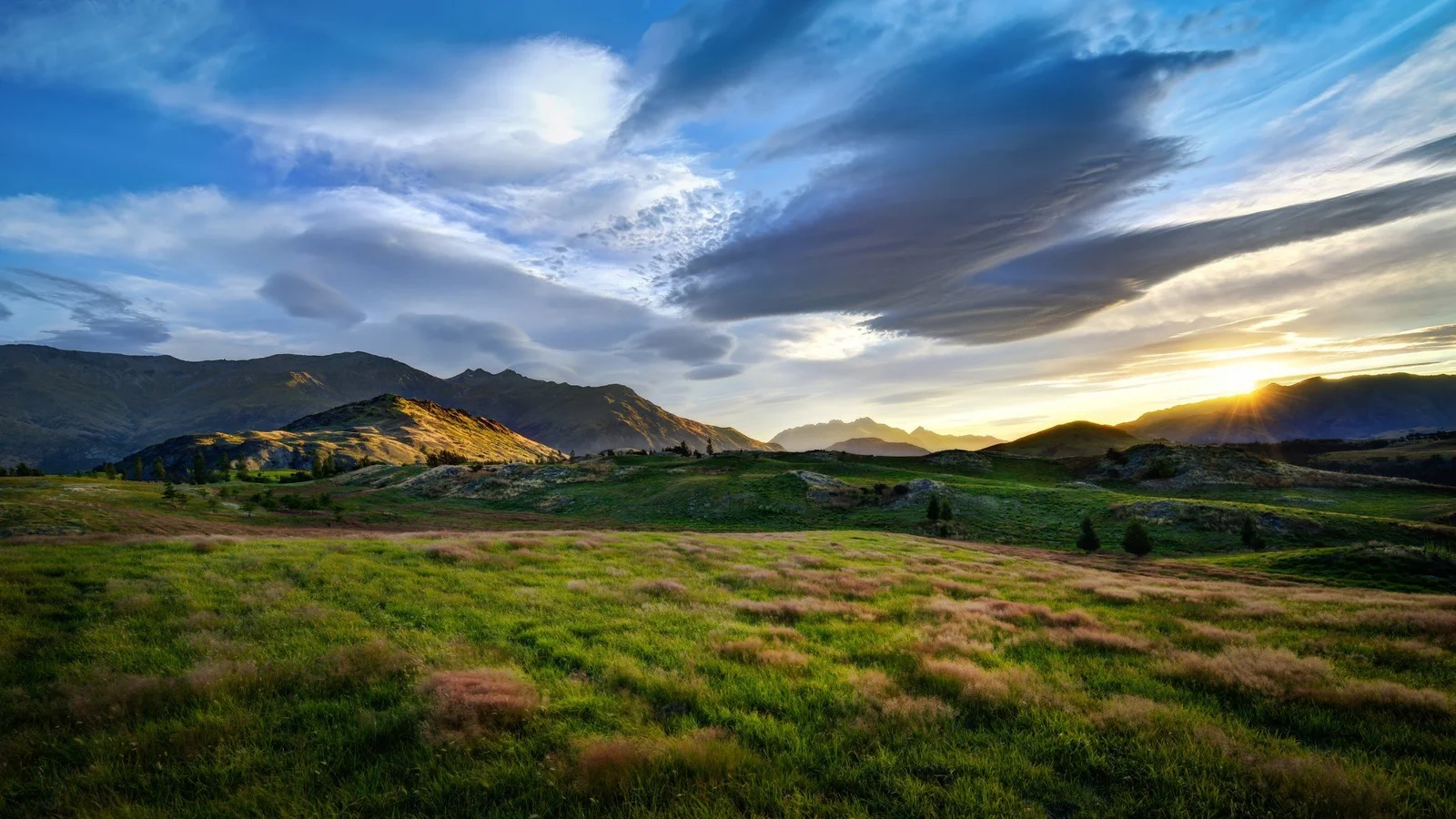 群山、草地与云层在夕阳下构成开阔的山谷风景。