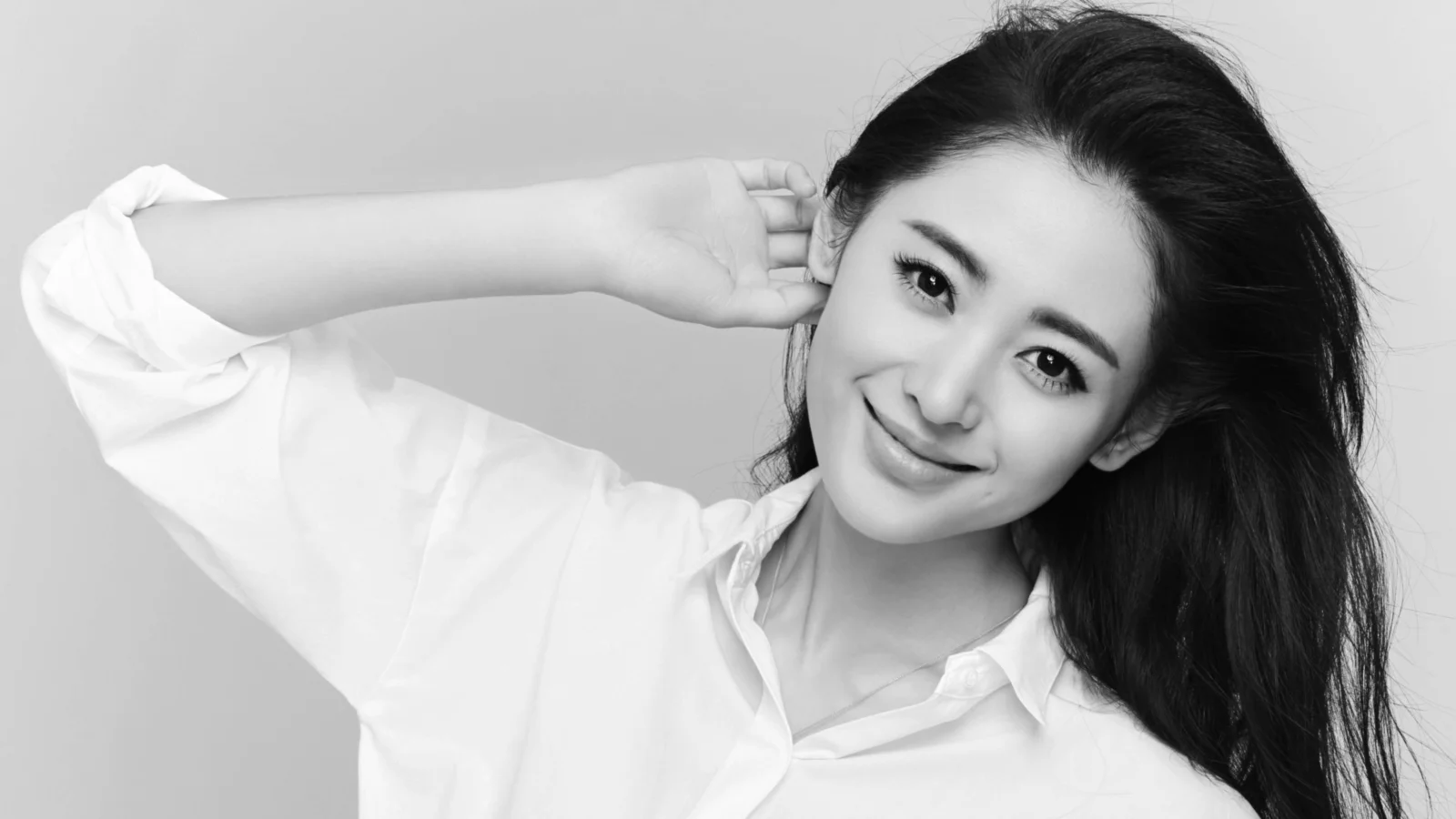 白いシャツを着た成人女性が、モノクロのポートレートでカメラに微笑みかけています。