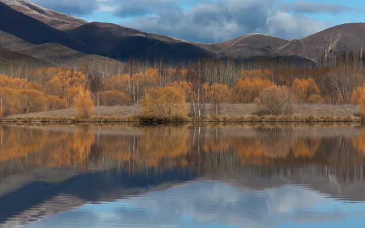 秋色树林、群山与宁静湖面倒映在一起，构成开阔的自然风景。