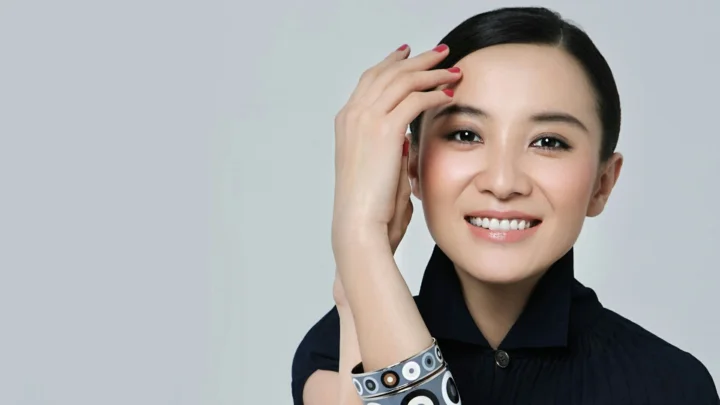 一位黑发女性在浅灰背景前微笑面对镜头。