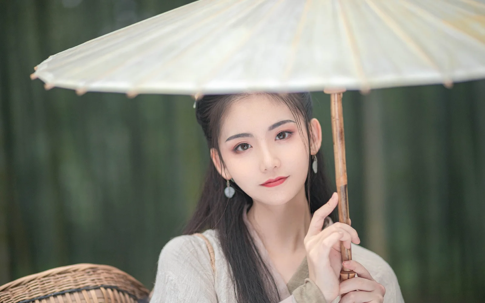 一名女子手持浅色伞站在深绿色背景前。