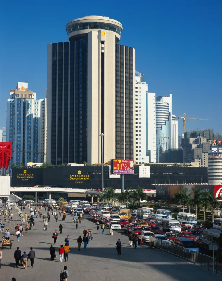蓝天下，高楼、酒店建筑、街道车辆和行人构成繁忙的城市街景。