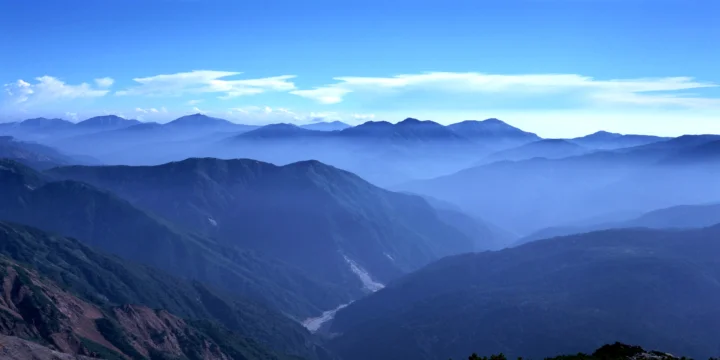 层叠的蓝色群山环绕着深邃峡谷，谷底可见一条蜿蜒的河流。