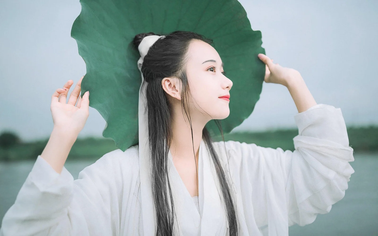 흰 옷을 입은 여성이 야외에서 연잎을 들고 있다.