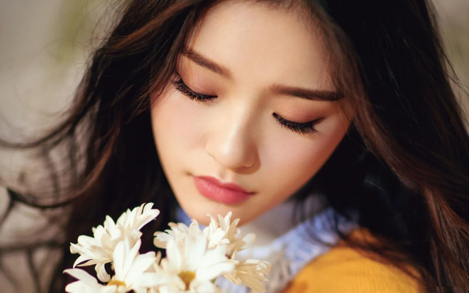 눈을 감은 성인 여성이 흰 꽃에 가까이 기대어 있고 긴 검은 머리카락이 화면 주변으로 펼쳐져 있습니다.
