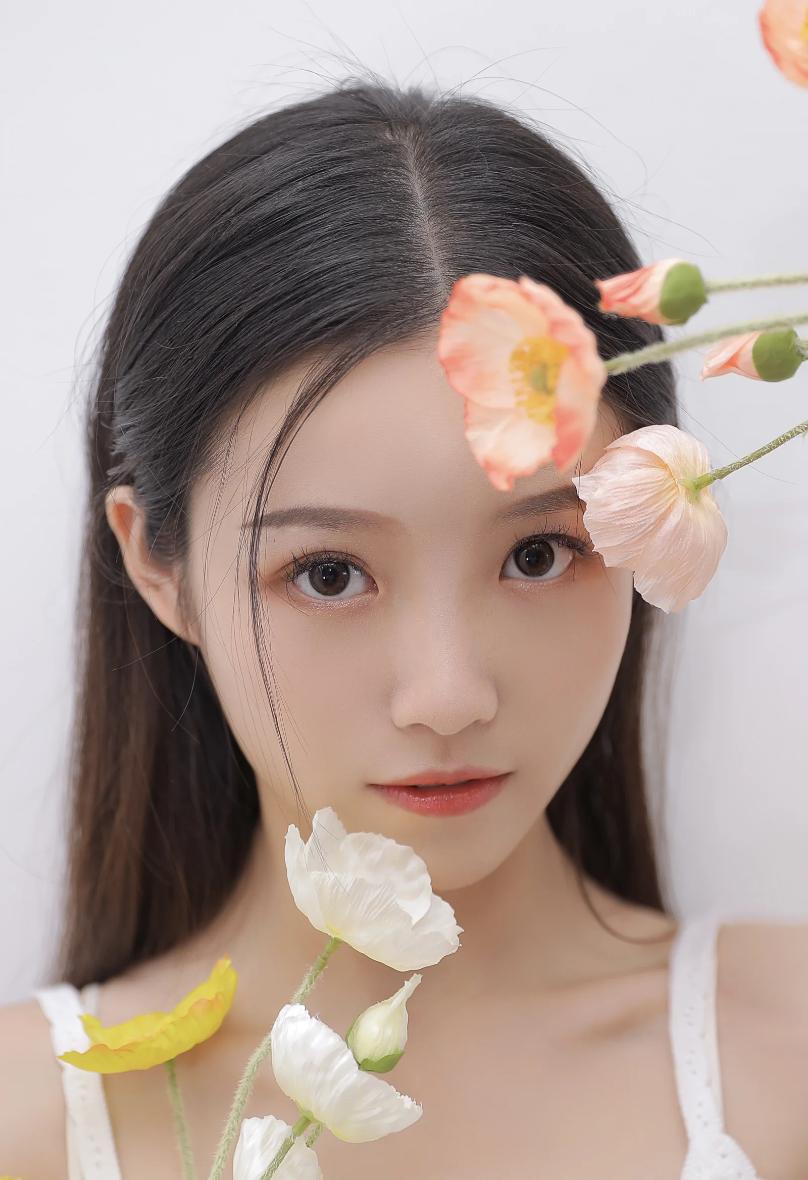 밝은 배경 앞에서 주황색과 흰색 꽃에 둘러싸인 성인 여성이 카메라를 바라보고 있습니다.