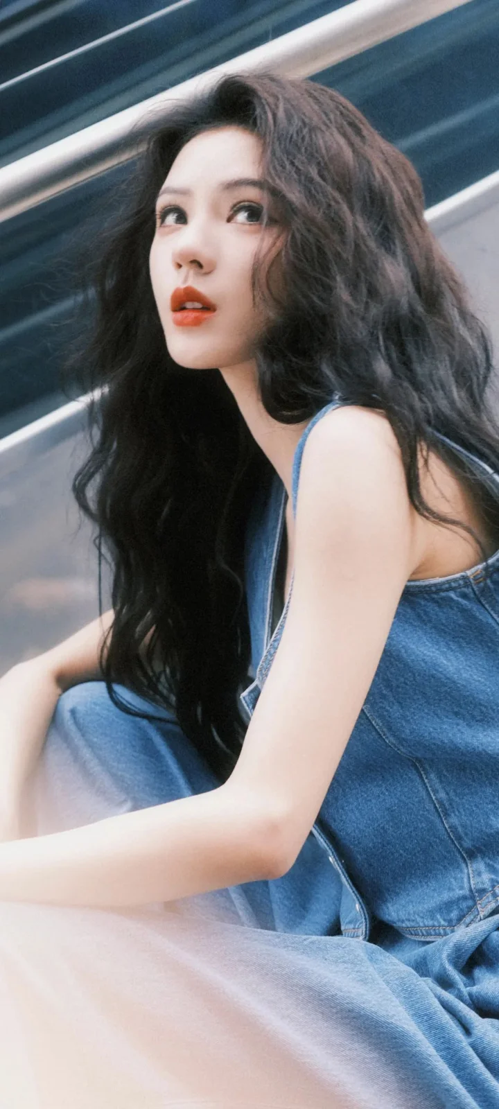 一名长发女性穿着蓝色牛仔服装坐着看向镜头外侧。