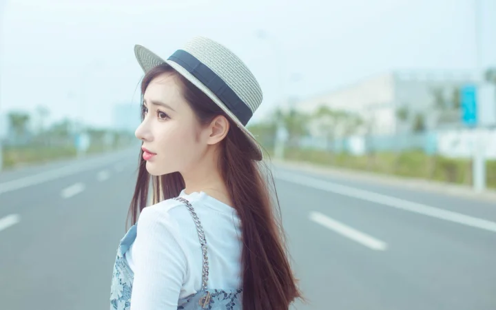一名戴着帽子的女子站在公路旁回望镜头。
