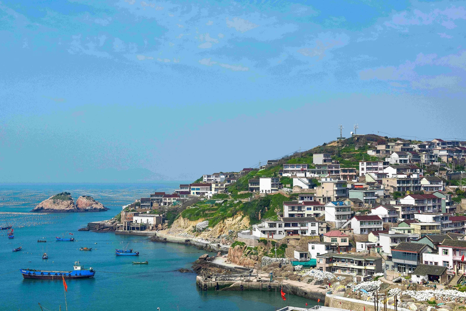 蓝色海湾旁的山坡上依海而建着密集的房屋，海面上停泊着几艘渔船。