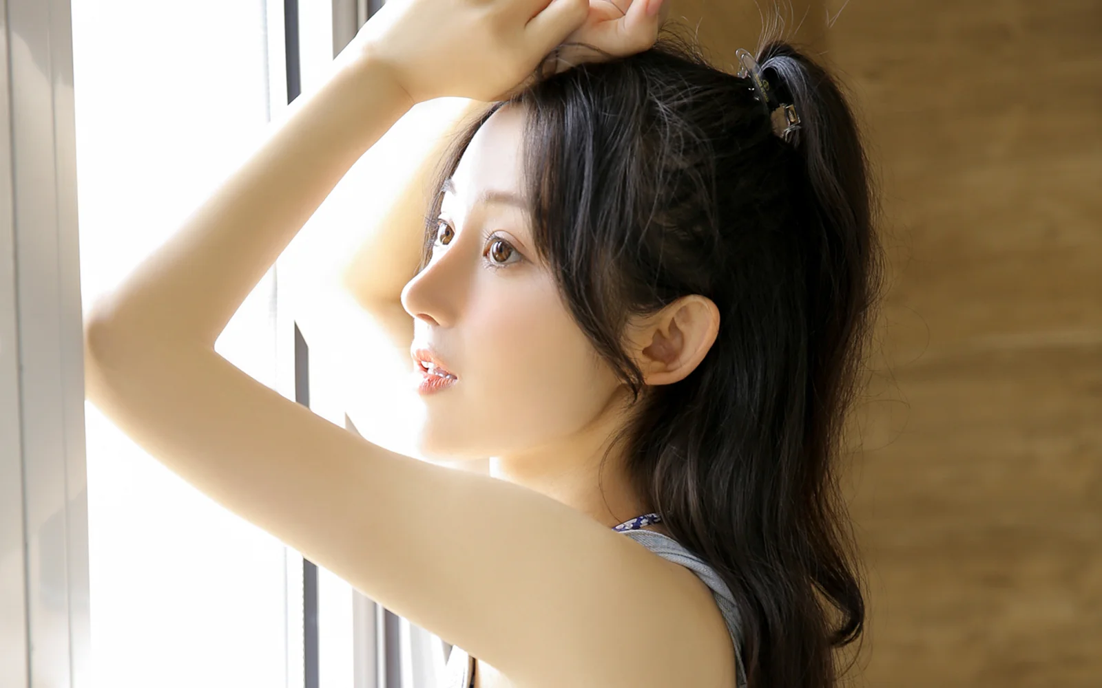 一名成年女性站在窗边，阳光照亮她的侧脸和深色长发。