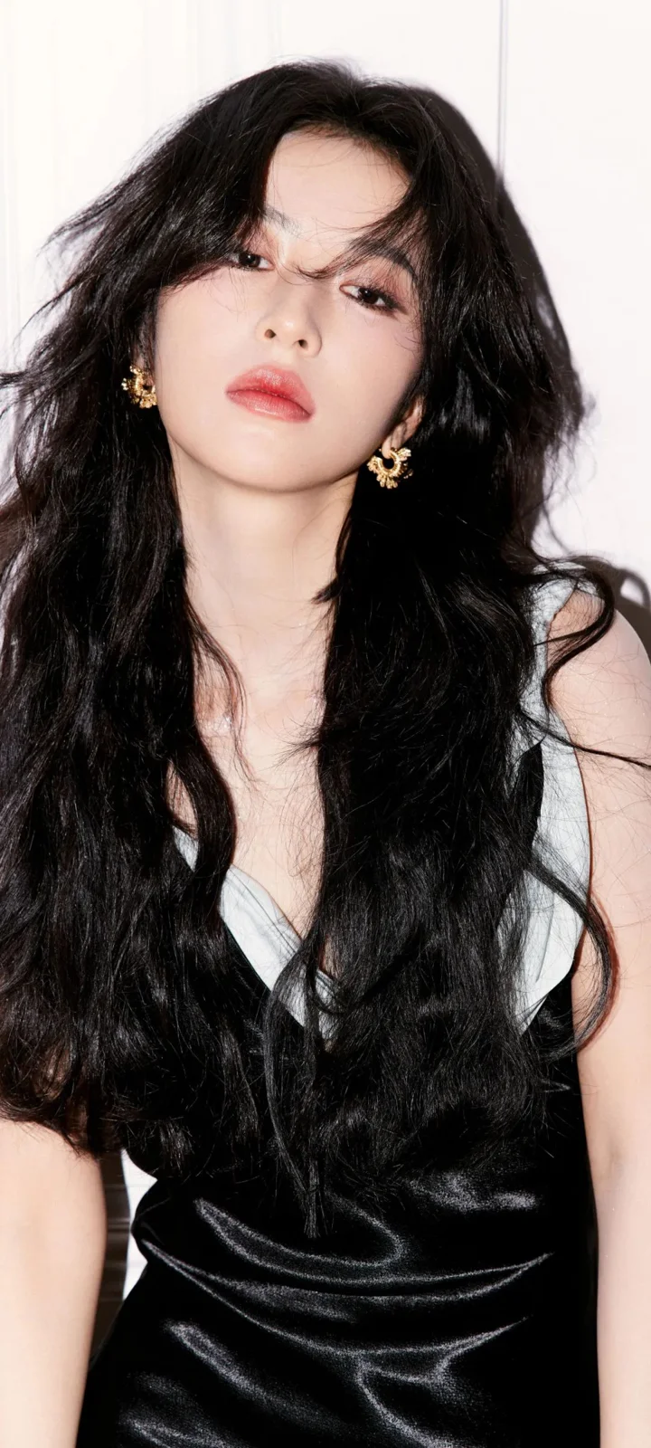 一位长发女性身穿黑色服装，在浅色背景前面对镜头。