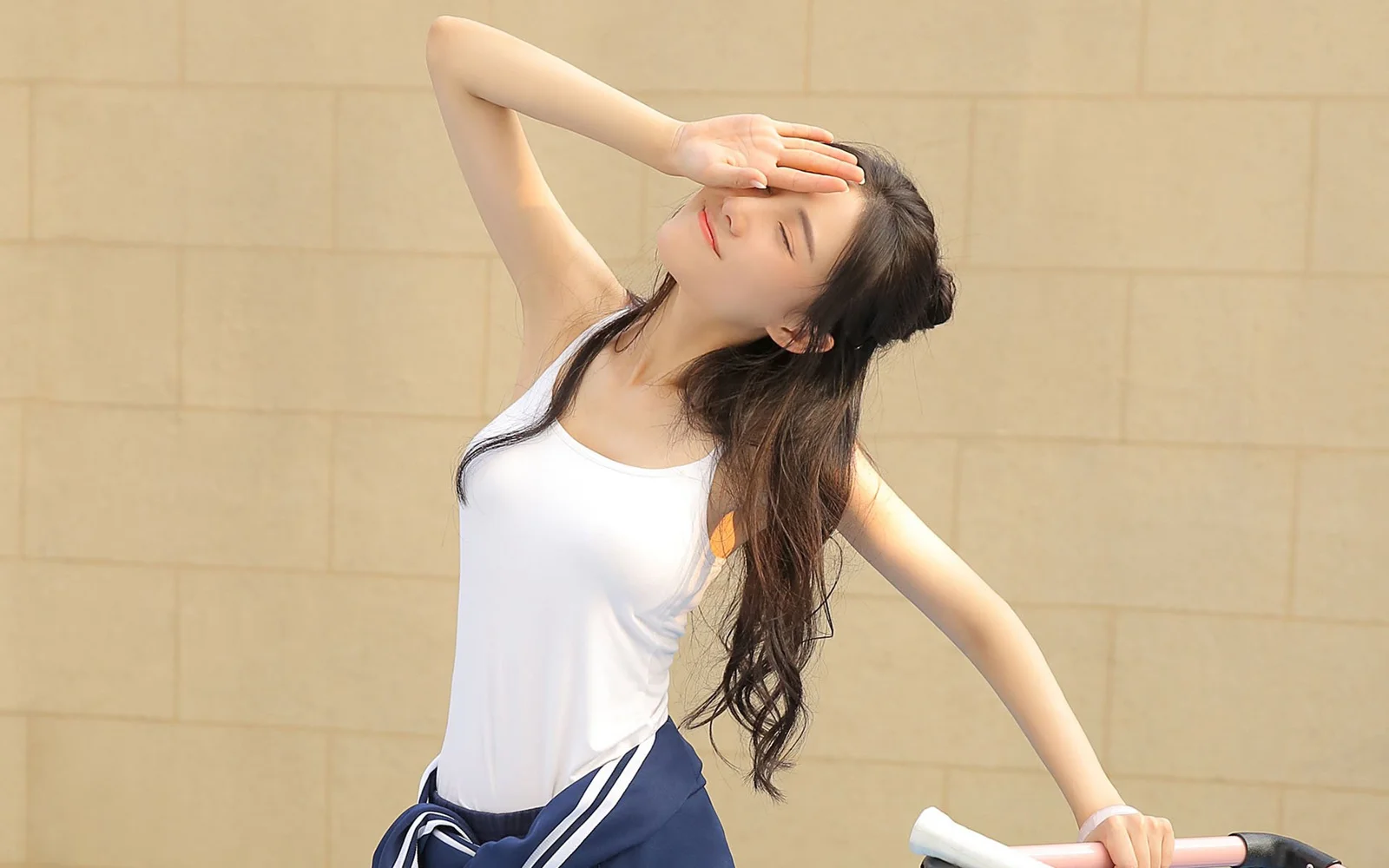 一名长发女子身穿白色背心，在浅色墙面前抬手遮光。