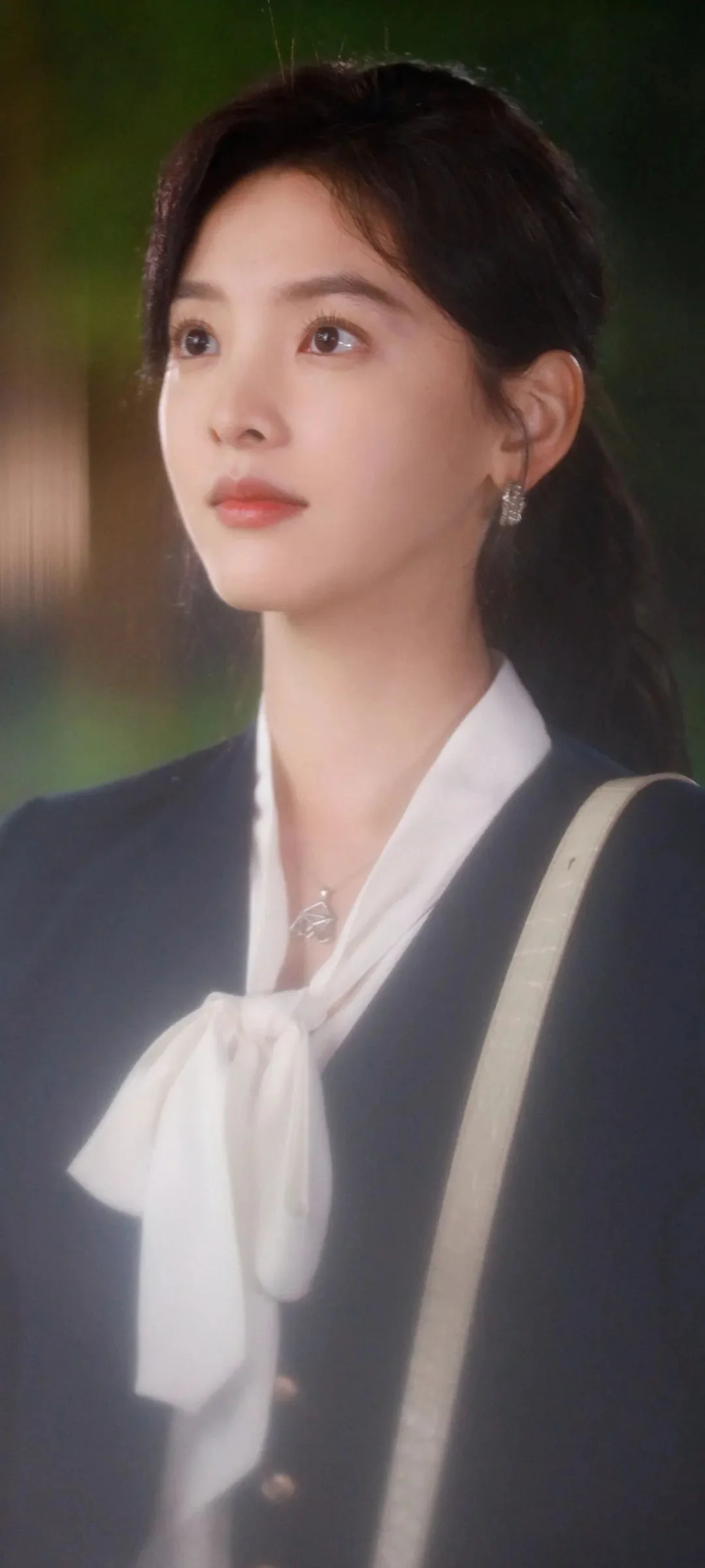 어두운 재킷과 흰색 리본 블라우스를 입은 여성의 초상으로, 배경은 부드럽게 흐려져 있습니다.