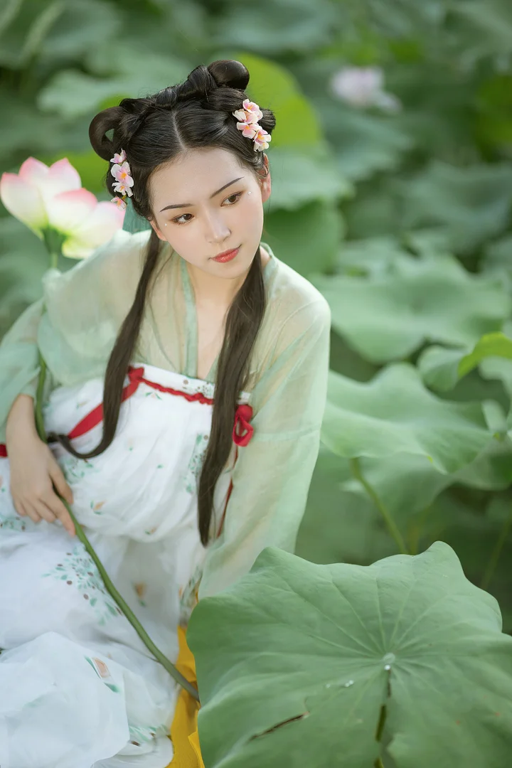 一名身穿传统服饰、头戴花饰的女子坐在荷花池边，周围是荷叶与盛开的荷花。