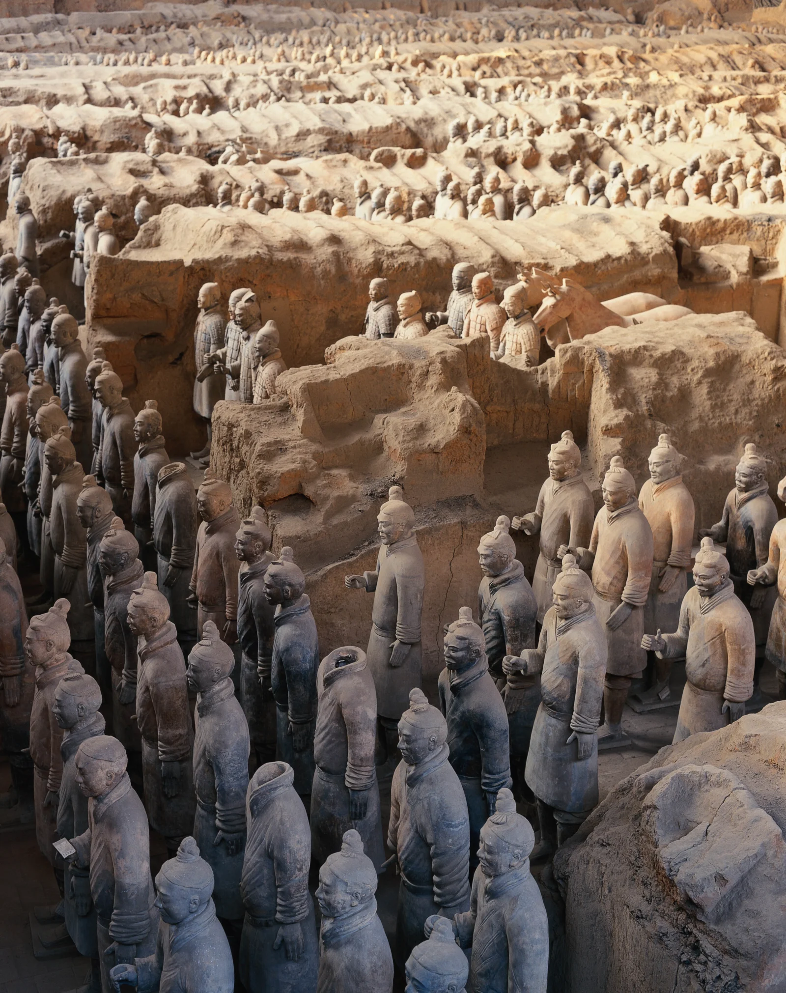 成排的兵马俑雕像陈列在土色坑道遗址中。