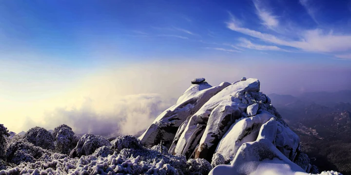 覆雪的山峰沐浴在蓝天与云海之间的柔和光线中。