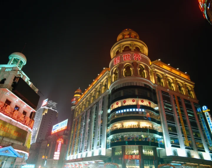 夜色中的城市建筑被霓虹灯和暖色灯光照亮，墙面与商铺上可见中文标牌。