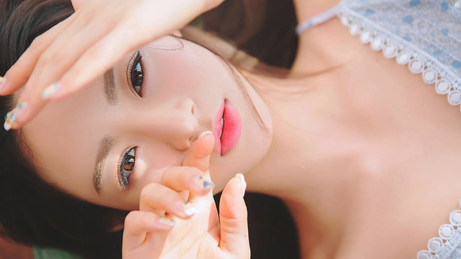 暗い背景を背に、両手を顔の近くに添えた成人女性のクローズアップポートレートです。