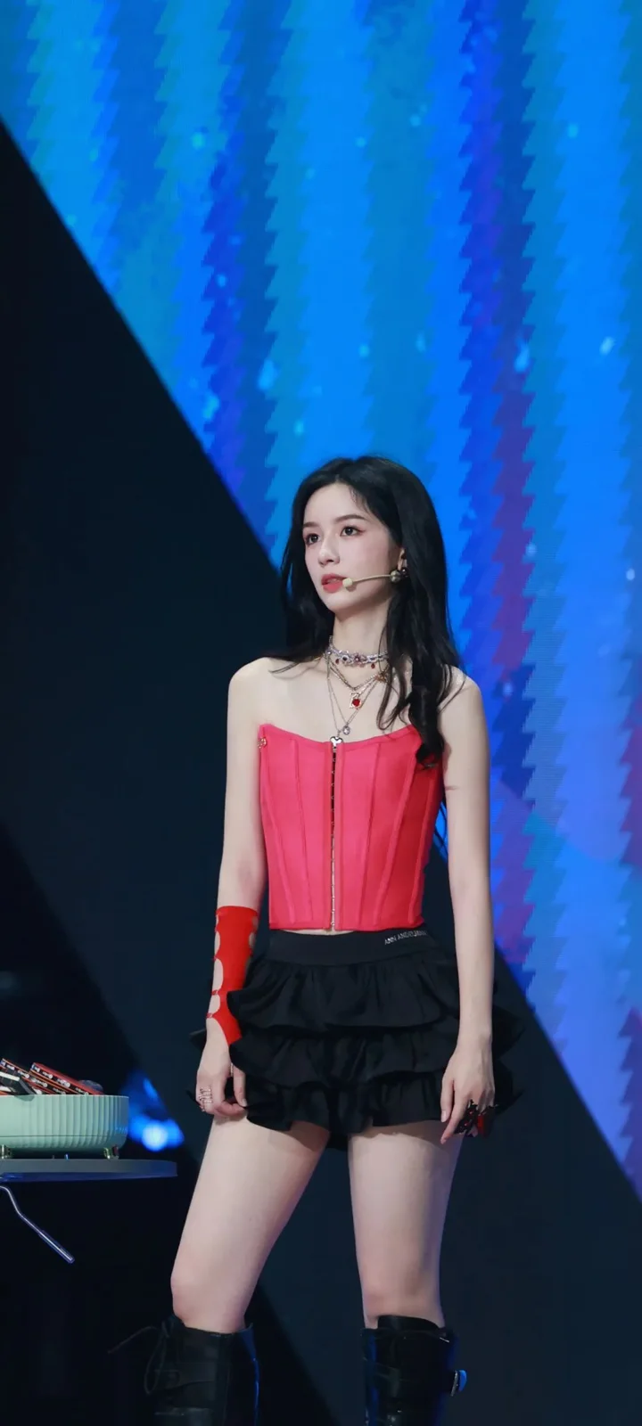 빨간 상의와 검은색 반바지를 입은 성인 여성이 푸른 조명의 무대에 서 있다.