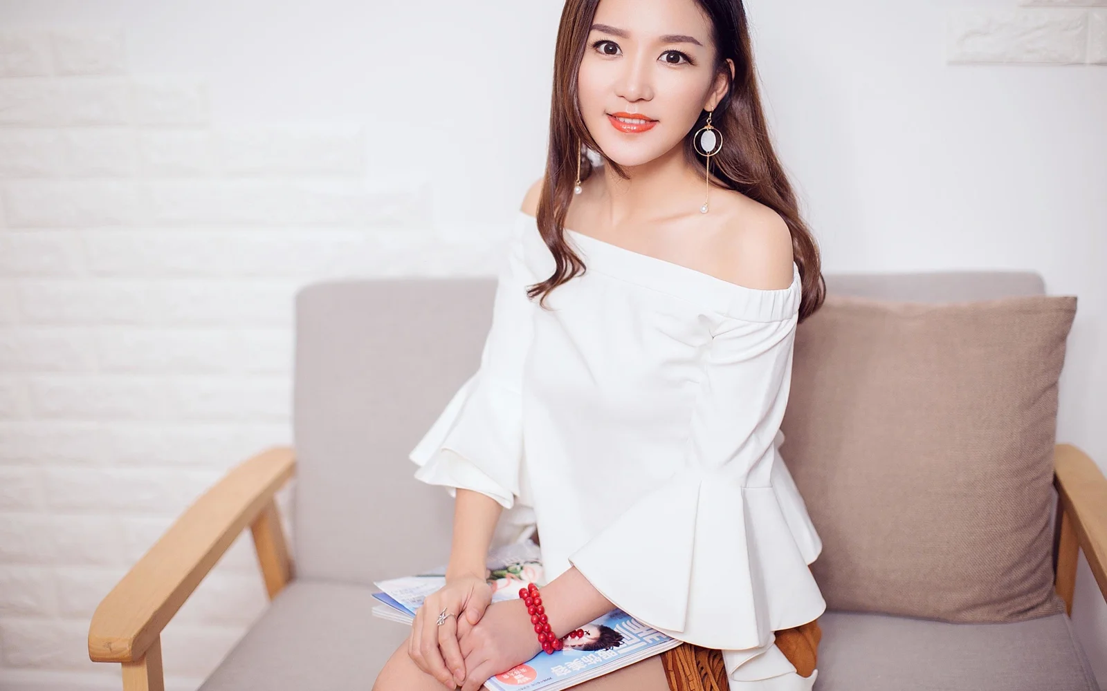 흰색 상의를 입은 성인 여성이 소파에 앉아 카메라를 향해 미소 짓고 있습니다.