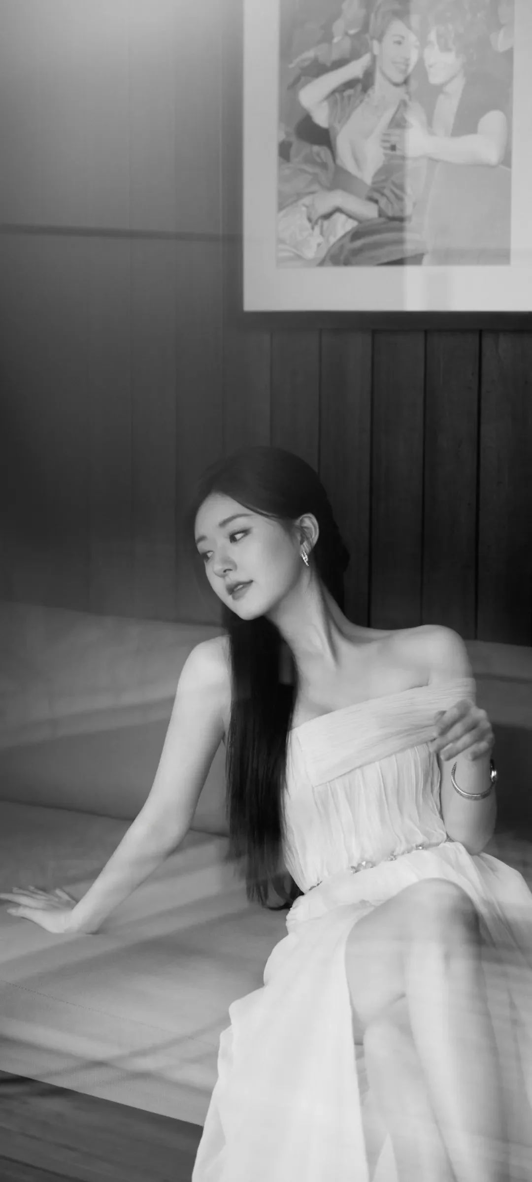 一位身穿白色连衣裙的女性坐在室内沙发上，画面呈黑白色调。