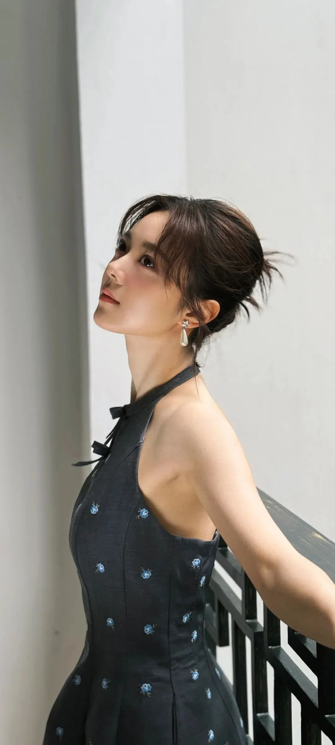 一位成年女子穿着黑色连衣裙站在楼梯旁，侧身望向上方。