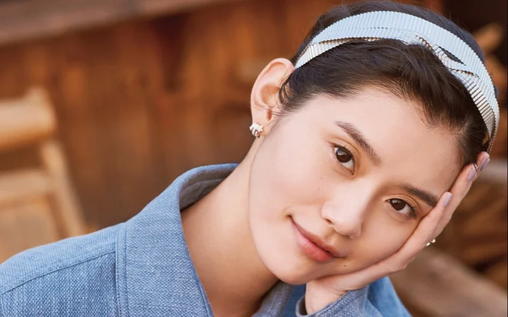 헤어밴드를 착용한 여성이 손에 얼굴을 기대고 미소 짓고 있다.