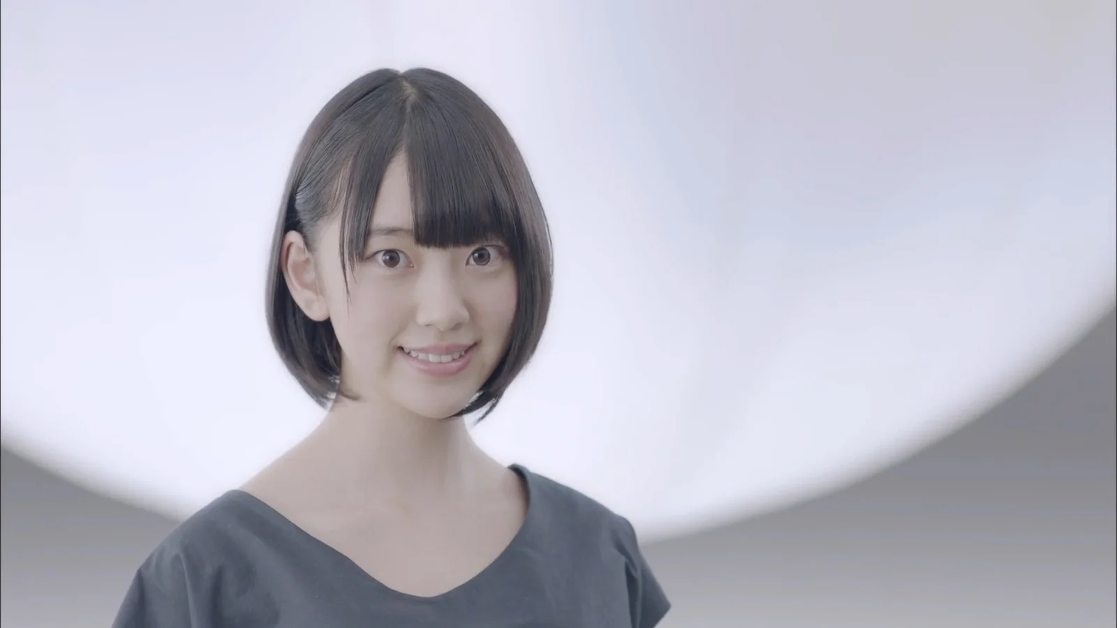 短い髪の女性が柔らかな明るい背景の前でカメラに向かって微笑んでいる。