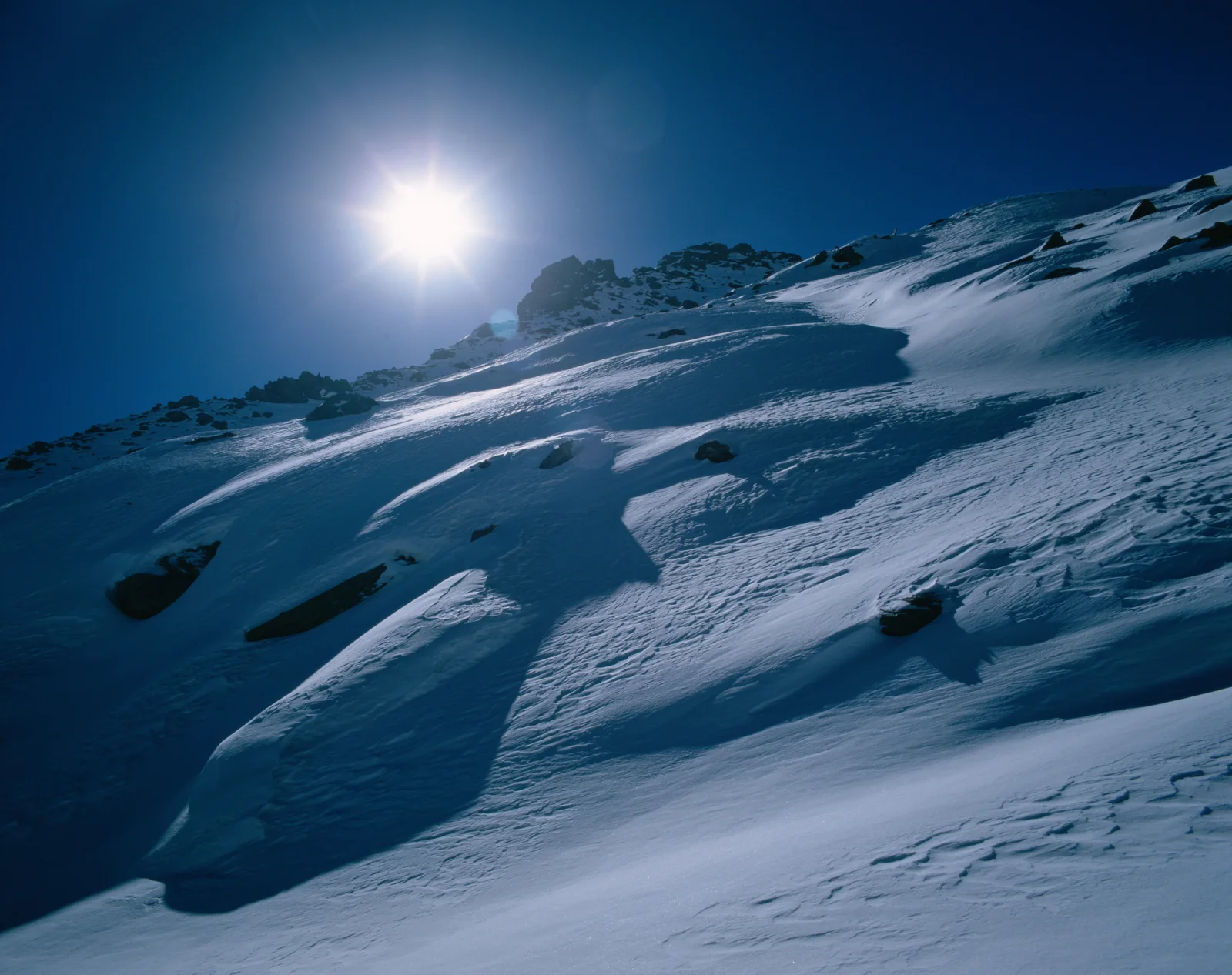 阳光照耀着覆雪的山坡，深蓝色天空映衬出清晰的雪地纹理。