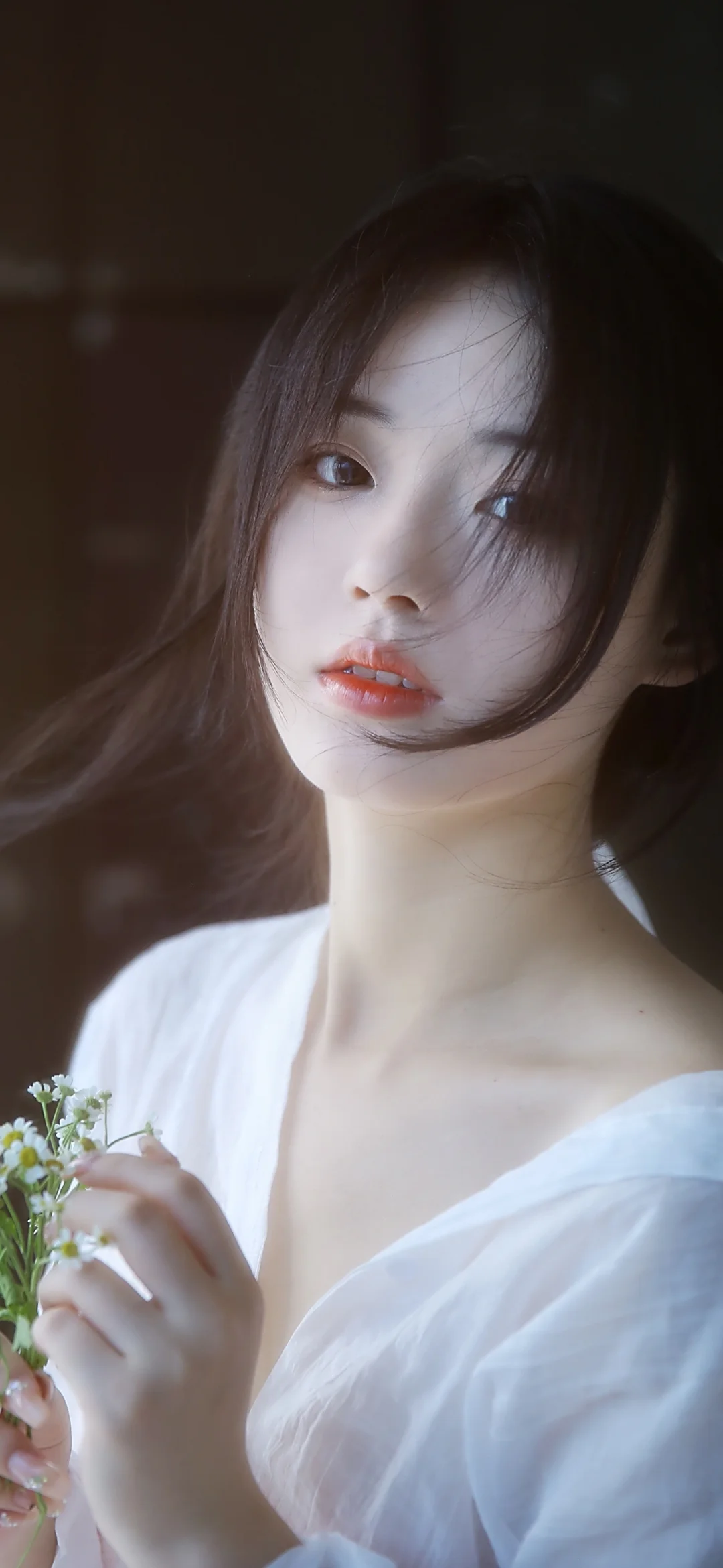 一名长发女子穿着白色上衣，手持小花进行近距离肖像拍摄。