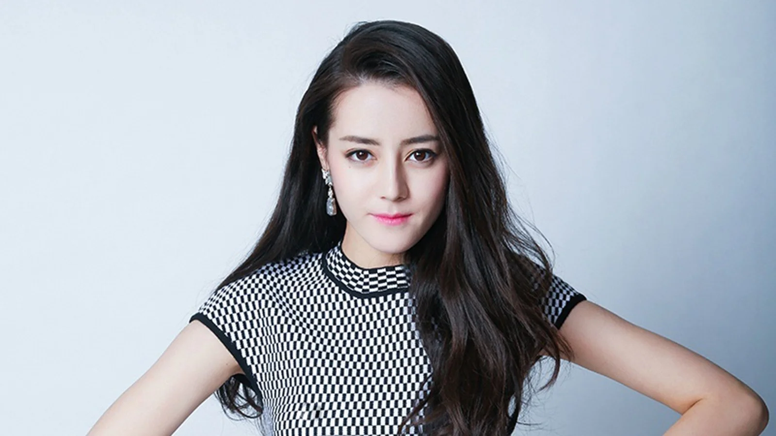 一名长发女性身穿黑白格纹上衣，在浅灰色背景前面对镜头微笑。