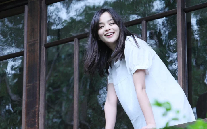 一名长发女子在木框窗边微笑。