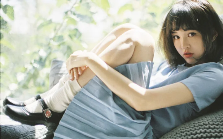 一名留着短发的女子穿着蓝色连衣裙坐在户外的柔和阳光中。