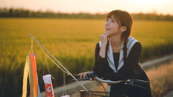 一名女子坐在自行车上，身后是夕阳下的金色田野。